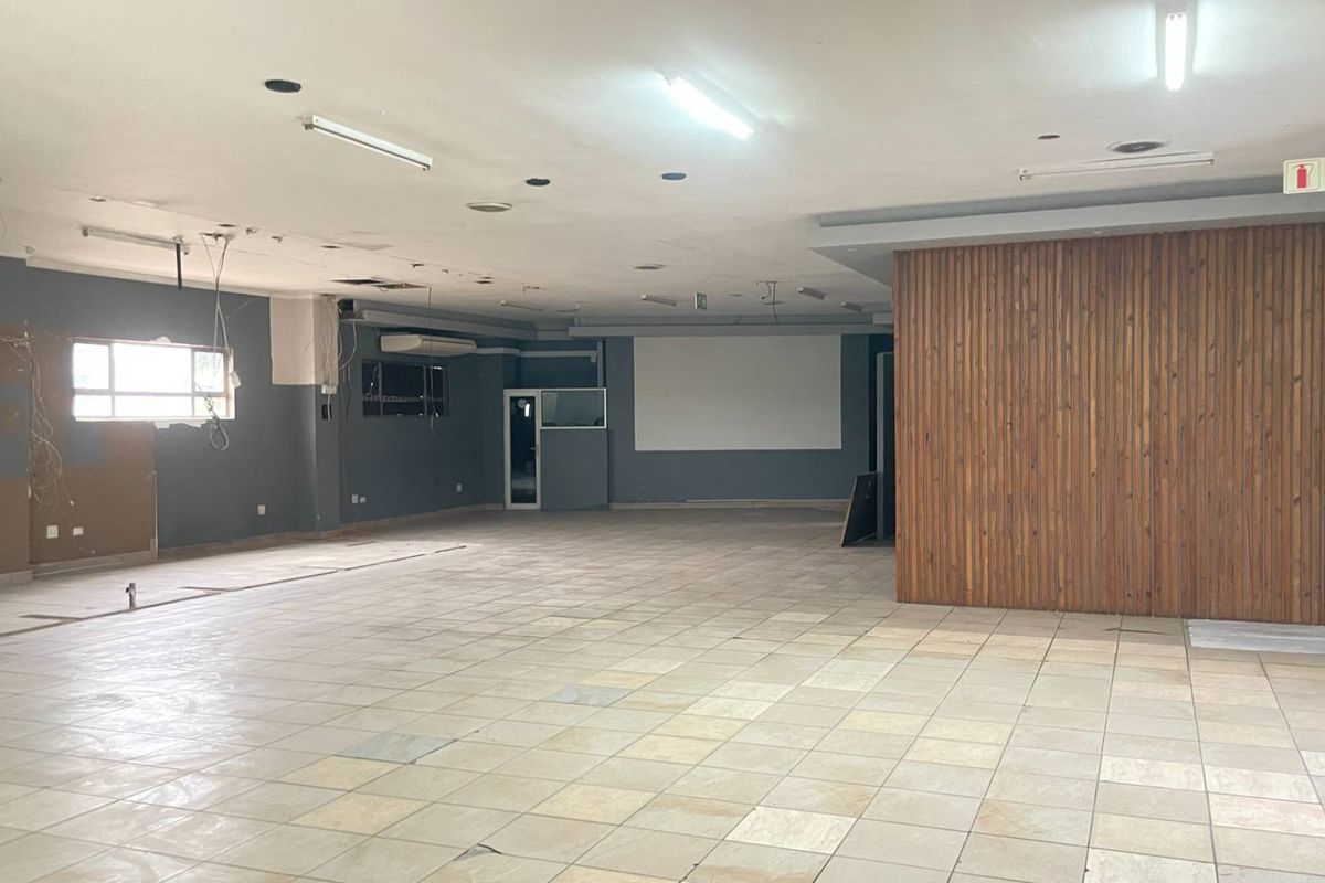 A large, vacant open-plan industrial space featuring tiled flooring, timber wall paneling, and fluorescent lighting, currently requiring maintenance and cosmetic updates.