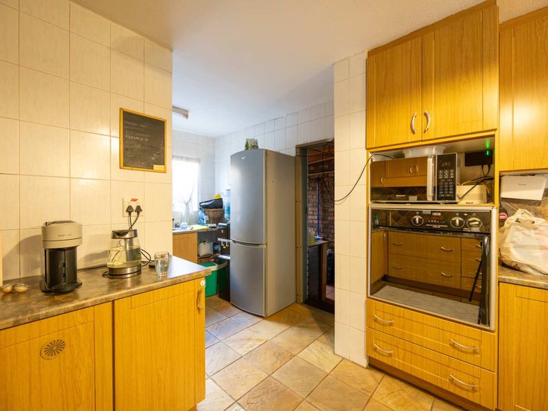 A functional kitchen featuring dated wood-look cabinetry, built-in oven, tiled splashbacks, and tiled flooring, offering potential for a modern renovation.