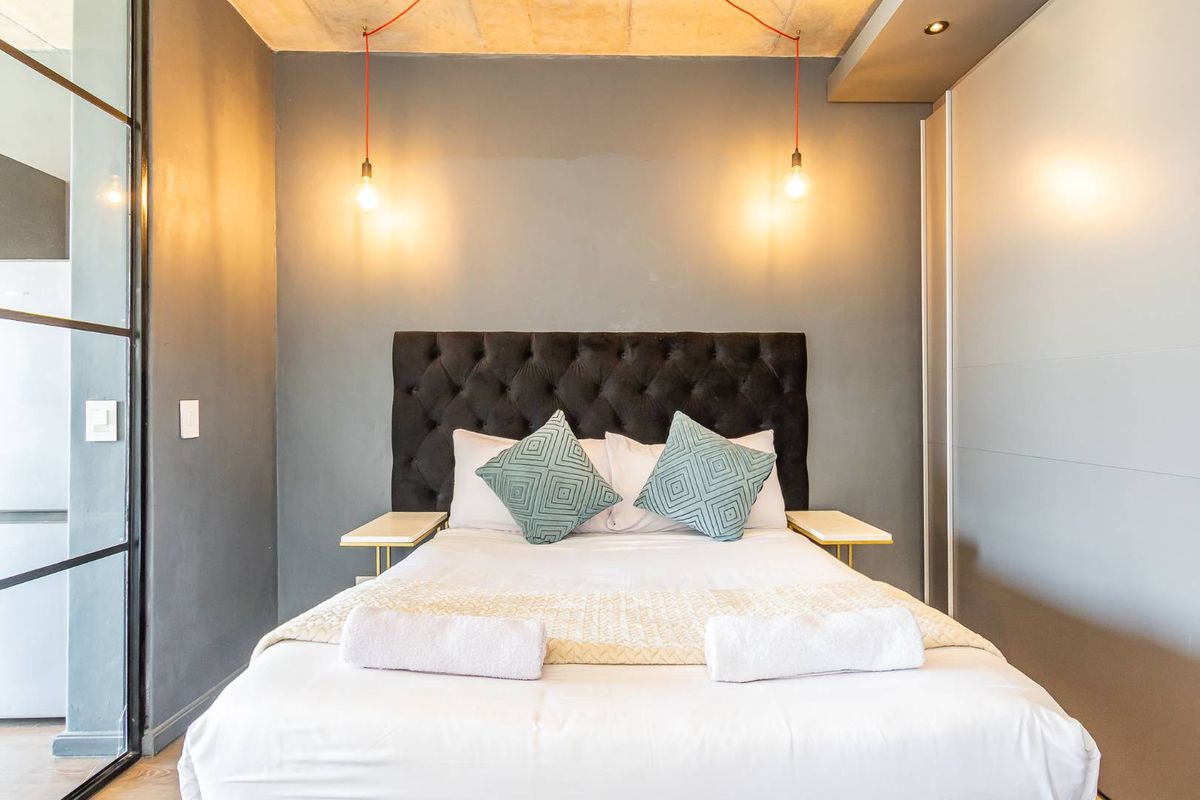 Modern bedroom featuring a concrete ceiling, built-in wardrobe, and industrial-style pendant lighting.