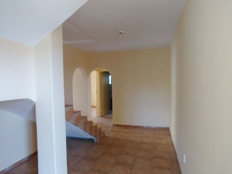 An empty hallway featuring tiled flooring, arched doorways, and a staircase leading to another level of the home.