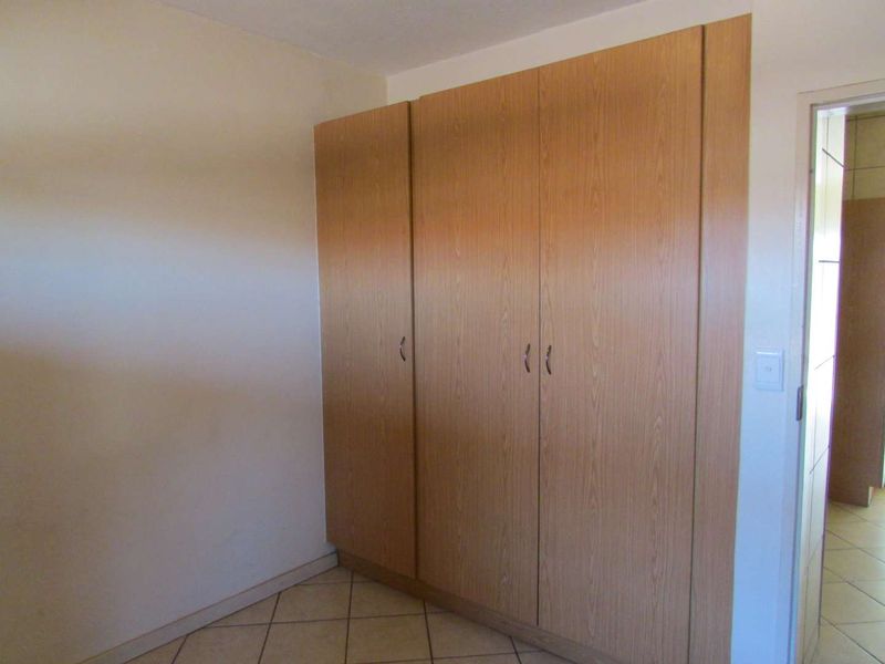A clean, empty bedroom featuring light wood-finish built-in cupboards and neutral tiled flooring.