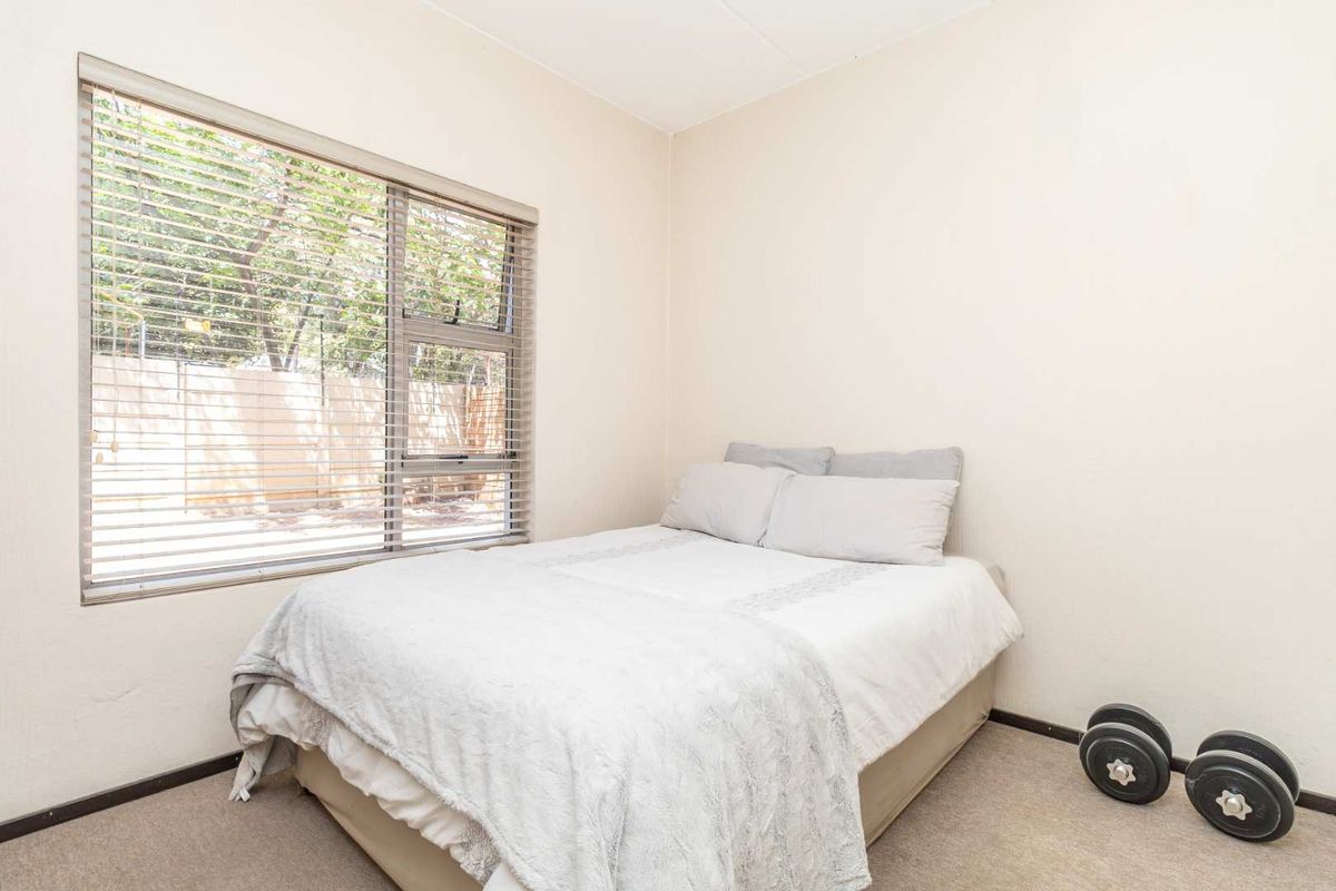 A functional bedroom featuring neutral wall finishes, carpeted flooring, and a large window with fitted blinds providing natural light.