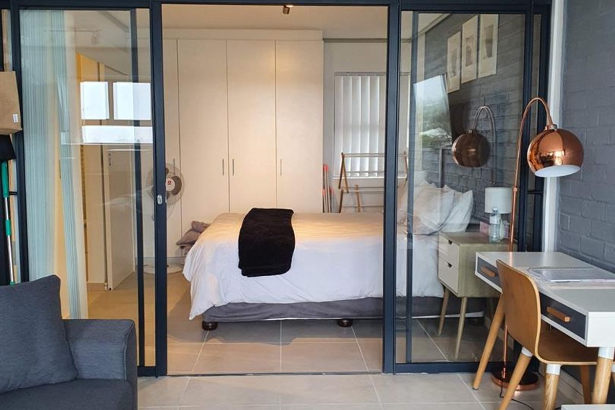 A modern bedroom featuring a sleek black-framed glass partition, built-in cupboards, and stylish exposed brick wall finishes, creating a contemporary and open living space.