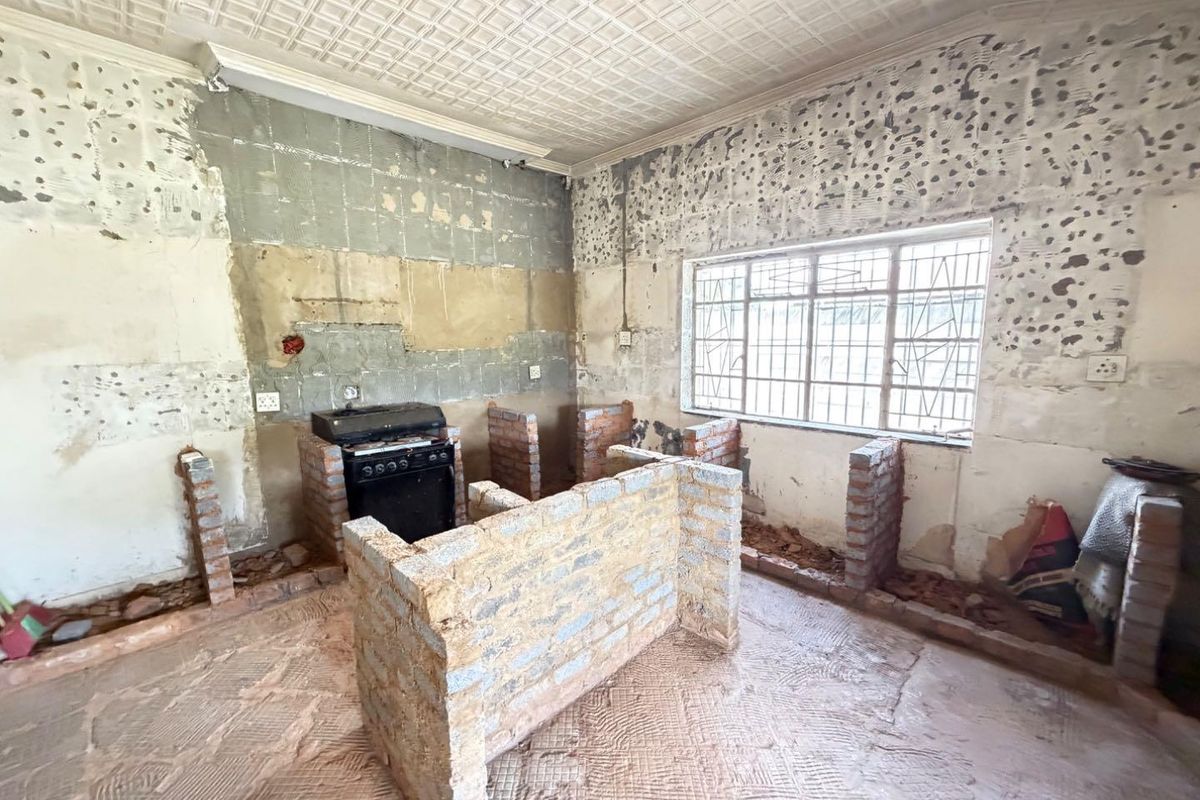 A kitchen space currently under renovation, featuring exposed brick structures, a freestanding stove, and unfinished wall and floor surfaces.