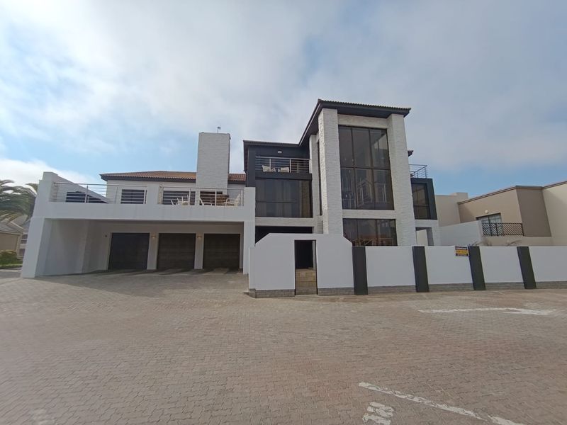 Modern multi-story residence featuring a triple garage, stone-clad facade, large glass windows, and a paved driveway entrance.