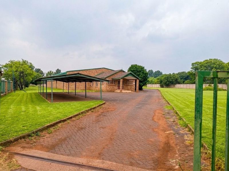 Front view of a commercial property featuring a brick building, a large carport, a paved driveway, and expansive lawn areas enclosed by boundary walls.