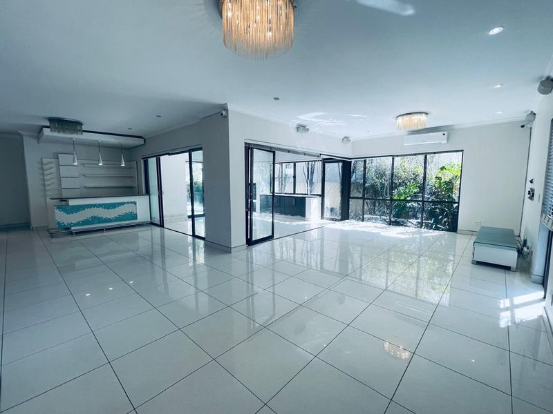 Spacious open-plan living area featuring polished tiled floors, a built-in bar, modern lighting, and large glass sliding doors opening to the exterior.