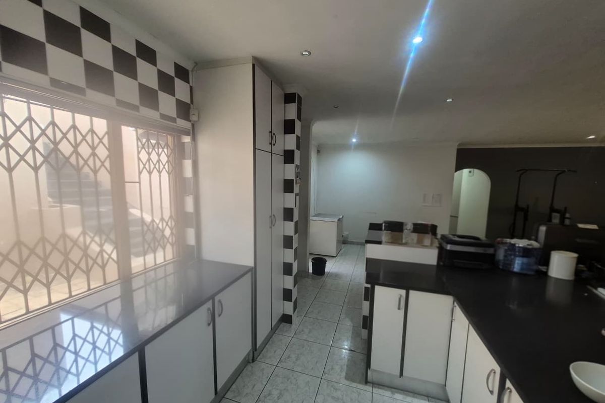 A functional kitchen featuring built-in cabinetry, dark stone countertops, and tiled flooring, with a security gate on the window.