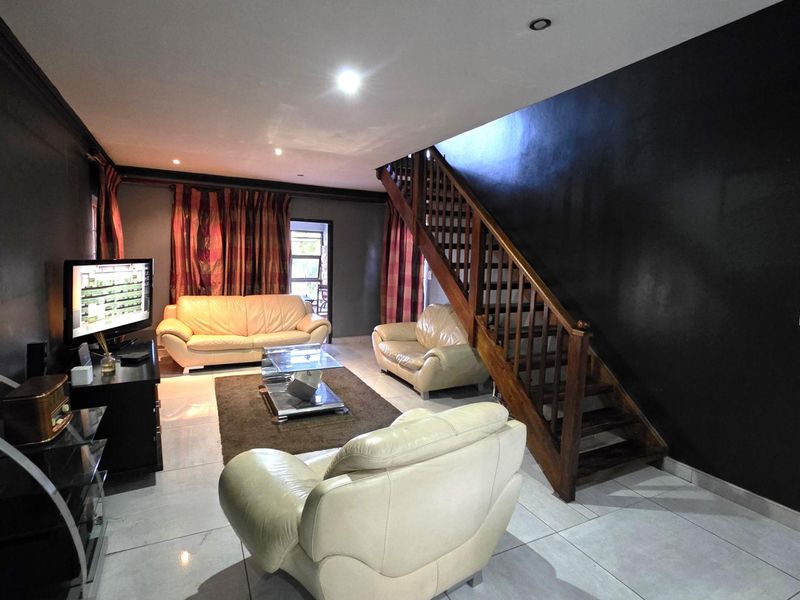 Spacious living room featuring tiled flooring, recessed lighting, and a prominent wooden staircase leading to the upper level.