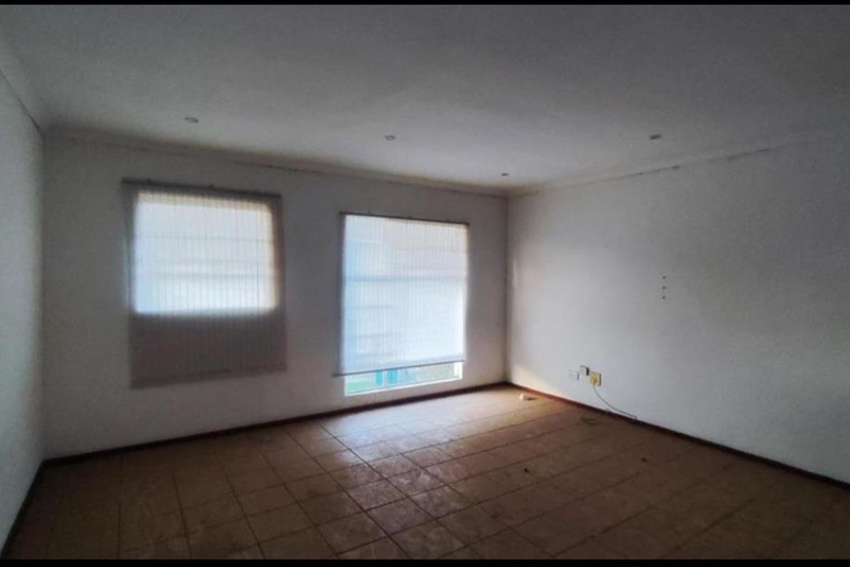 An empty living room featuring tiled flooring, recessed ceiling lighting, and two windows fitted with roller blinds.
