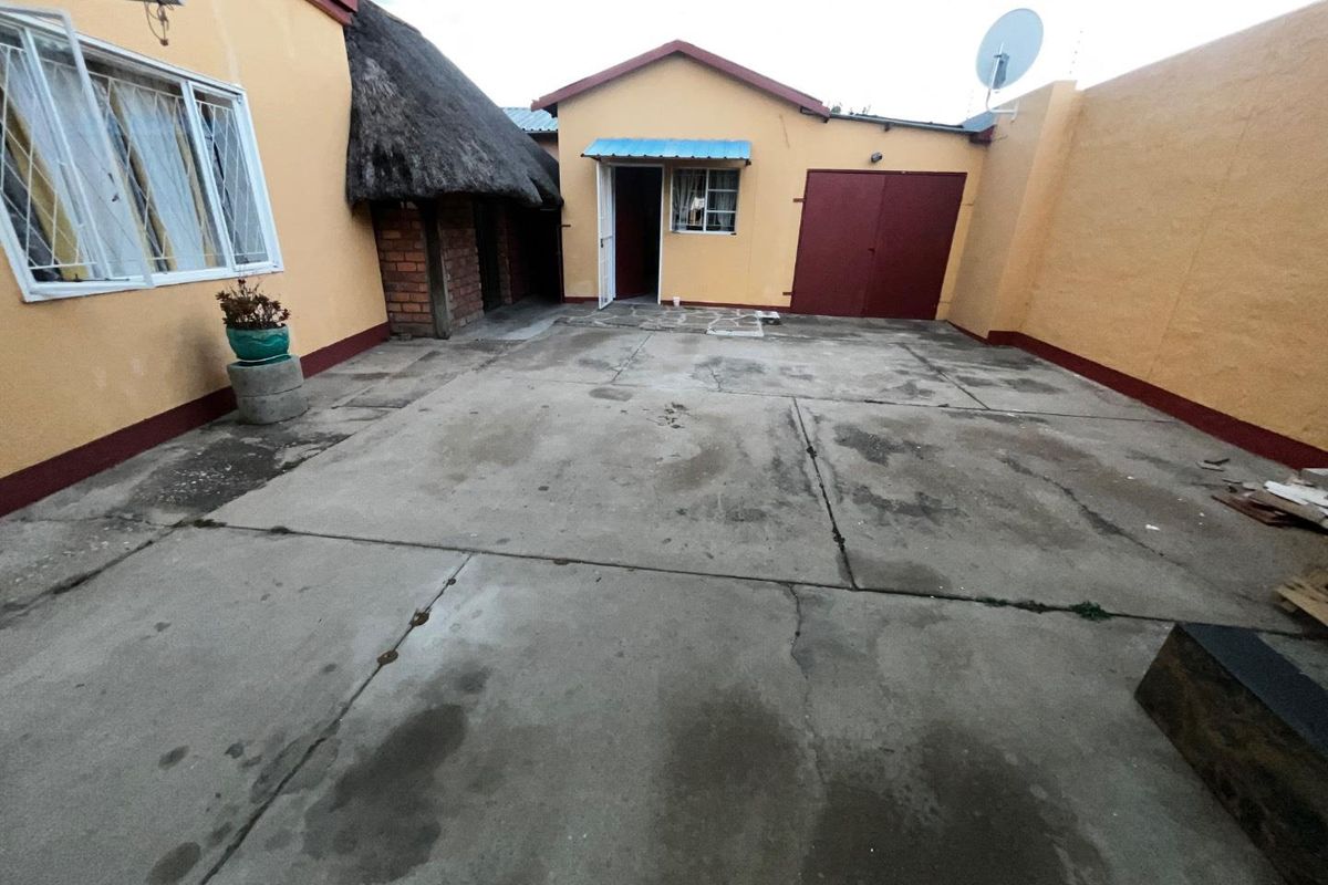 A paved rear courtyard area featuring a thatched structure, solid boundary walls, and access to the main dwelling and garage.