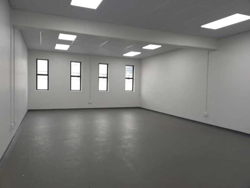 A spacious, empty industrial office area featuring neutral walls, painted concrete flooring, and recessed ceiling lighting, providing a clean and versatile workspace.