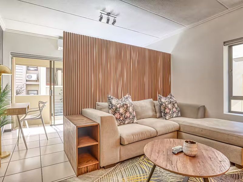 A modern living area featuring a stylish slatted timber partition wall, tiled flooring, and direct access to a balcony through a sliding glass door.