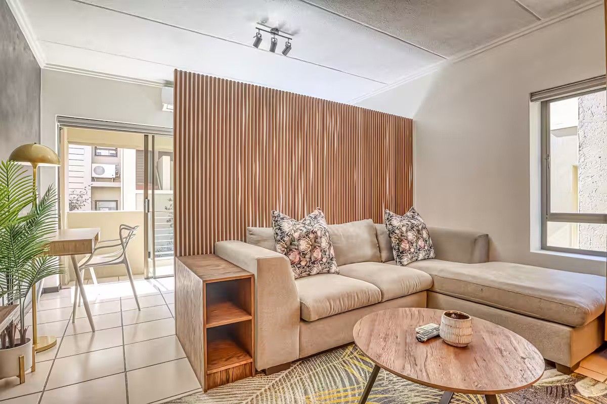 A modern living area featuring a stylish slatted timber partition wall, tiled flooring, and direct access to a balcony through a sliding glass door.