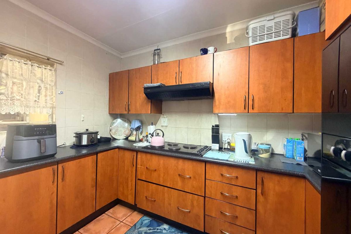 A functional kitchen featuring wooden cabinetry, dark laminate countertops, a built-in electric hob with extractor fan, and tiled finishes throughout.