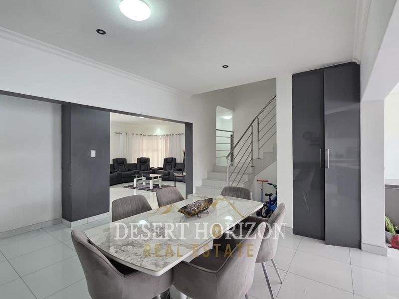 Open plan dining area featuring modern tiled flooring, recessed lighting, and a staircase with a stainless steel balustrade leading to the upper level.