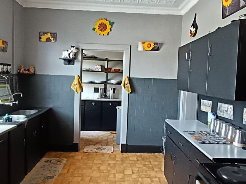 A functional kitchen featuring dark cabinetry, tiled splashbacks, and an adjoining scullery area, providing practical storage and preparation space.