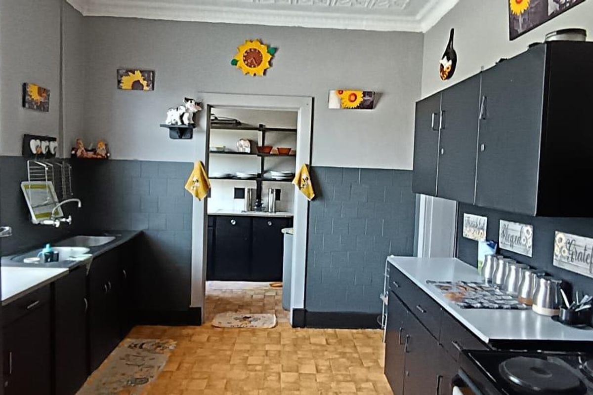A functional kitchen featuring dark cabinetry, tiled splashbacks, and an adjoining scullery area, providing practical storage and preparation space.