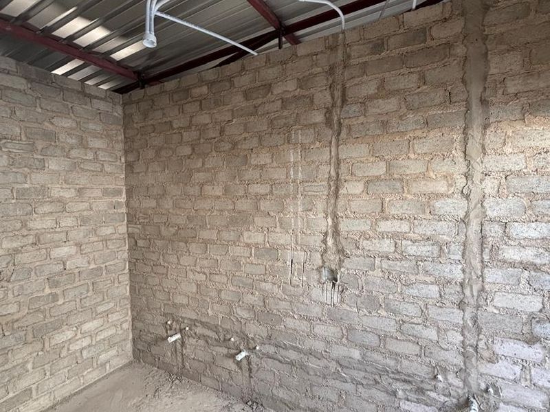 An unfinished utility space featuring exposed brick walls, concrete flooring, and exposed plumbing and electrical infrastructure, ready for completion.
