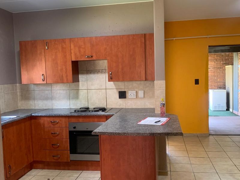 A functional kitchen featuring wooden cabinetry, granite countertops, built-in oven and hob, with tiled flooring and backsplash throughout.