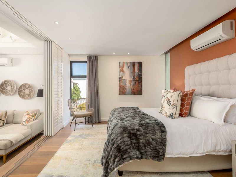 A well-appointed bedroom featuring timber flooring, recessed lighting, a split-system air conditioner, and a folding partition connecting to an adjacent living space.