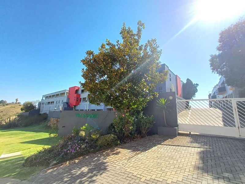 The front entrance of The Summit apartment complex, featuring a paved driveway, secure gated access, and well-maintained landscaped garden areas.