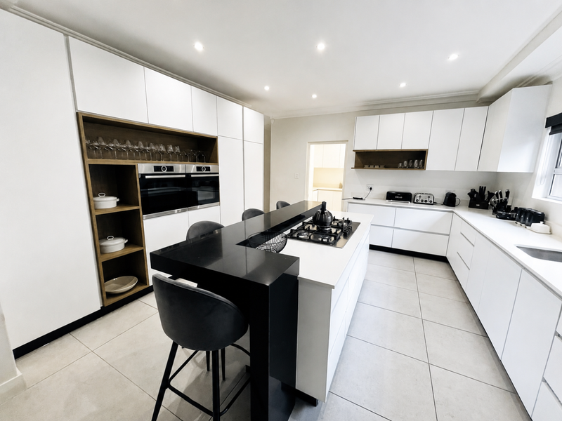 Modern, high-end kitchen featuring sleek white cabinetry, a central island with a black stone breakfast bar, gas hob, and integrated double ovens.