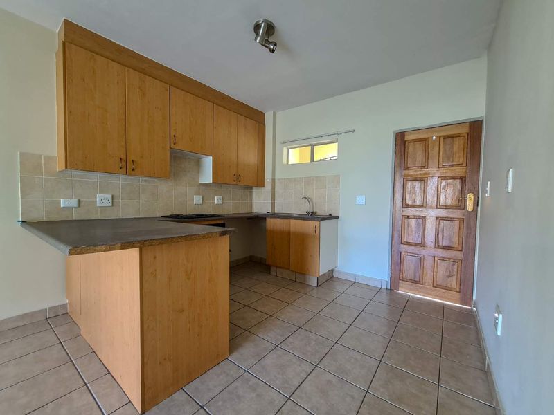 A functional kitchen featuring laminate cabinetry, tiled backsplash, built-in hob, and ceramic floor tiles, offering a clean and practical layout.