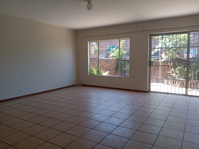 Spacious, empty living area featuring neutral tiled flooring, large windows, and a sliding glass door with security gate leading to the exterior.