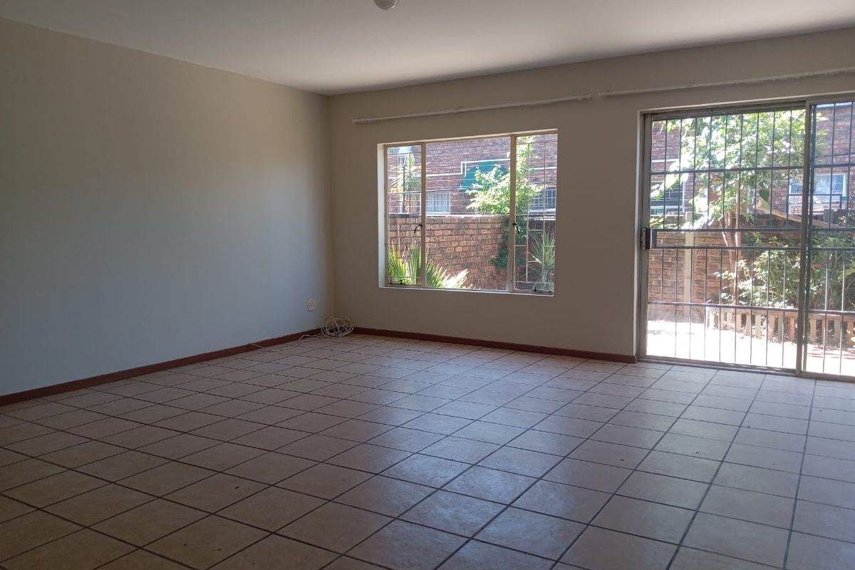 Spacious, empty living area featuring neutral tiled flooring, large windows, and a sliding glass door with security gate leading to the exterior.