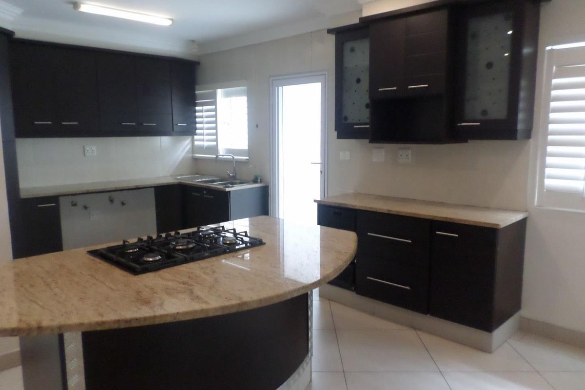 Modern kitchen featuring dark cabinetry, granite countertops, a central island with a built-in gas hob, and tiled flooring.