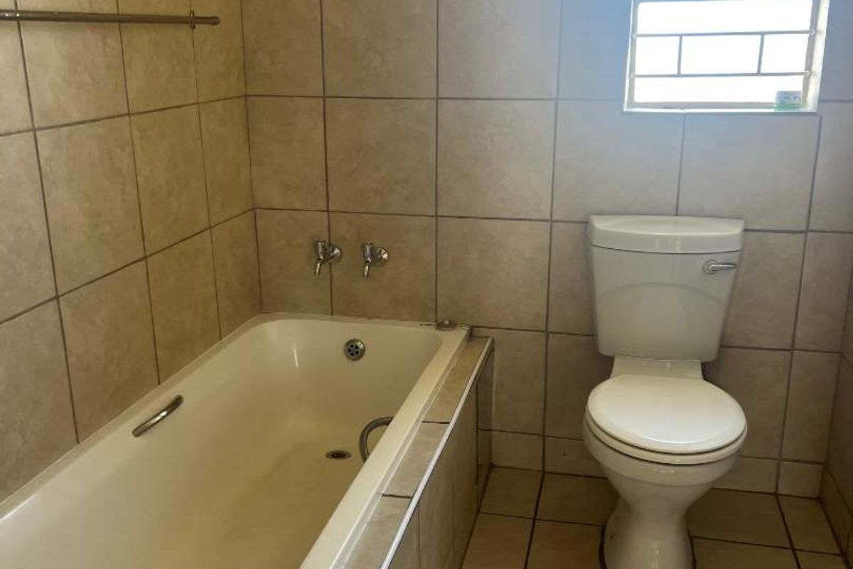 A functional bathroom featuring a built-in bathtub with tiled surround, a standard toilet, and tiled flooring with a decorative border.