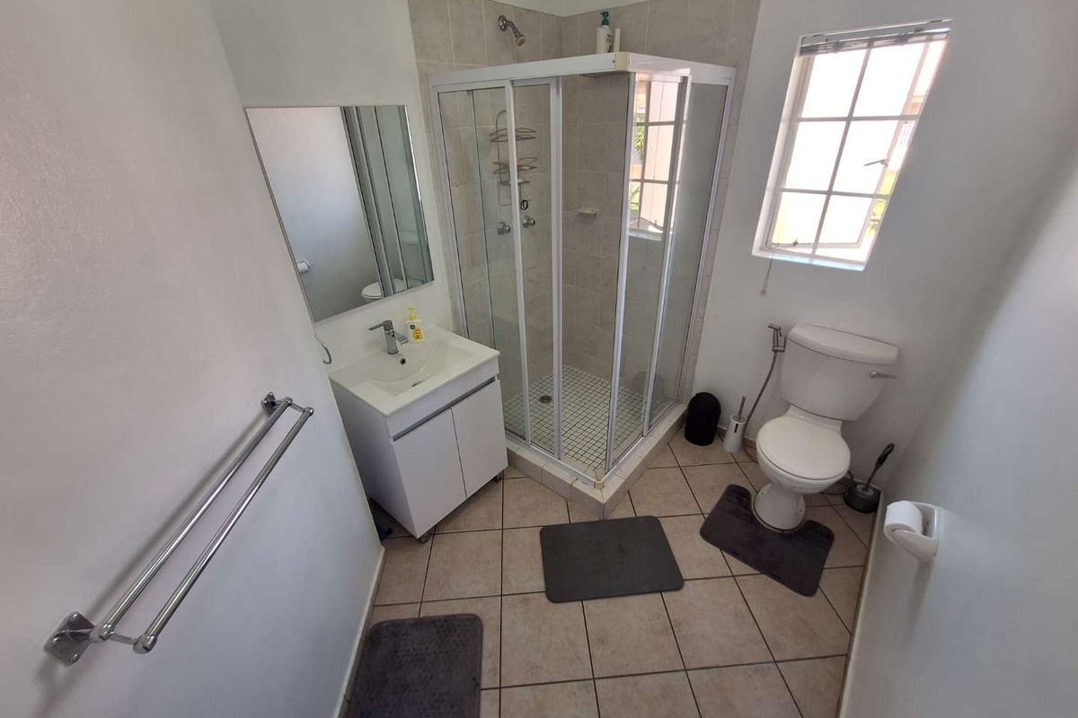A functional bathroom featuring a corner shower enclosure, a vanity basin with storage, a toilet, and tiled flooring with natural light from a window.