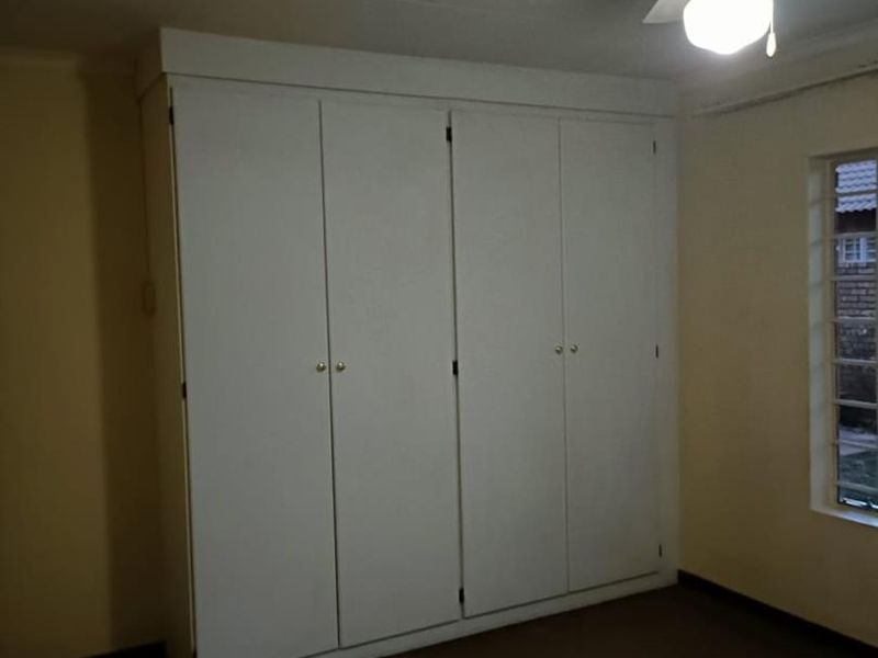A bedroom featuring built-in cupboards, a ceiling fan, and a window with security bars.
