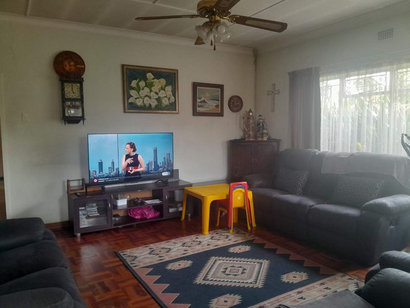 A living room featuring traditional parquet flooring, a ceiling fan, and large windows with security gates, offering a functional and lived-in space.