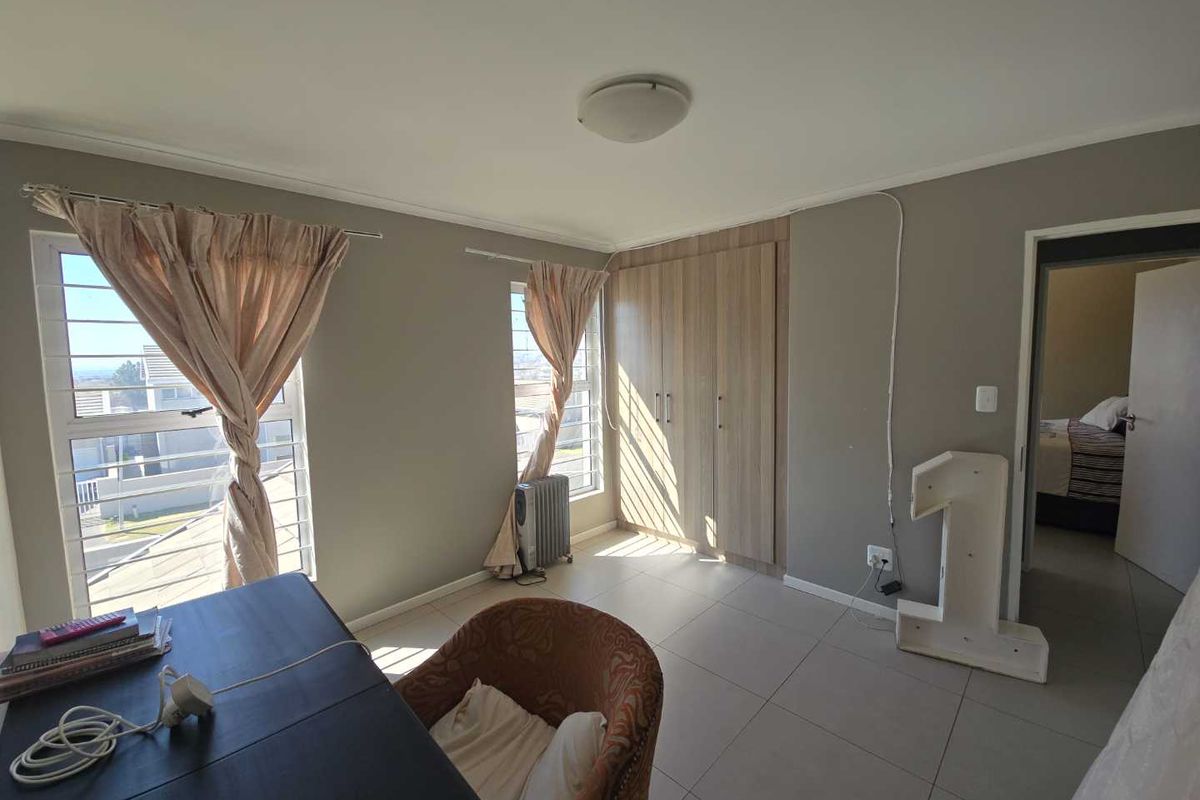 A bedroom featuring tiled flooring, built-in wooden cupboards, and aluminium window frames, offering a functional space with neutral wall tones.