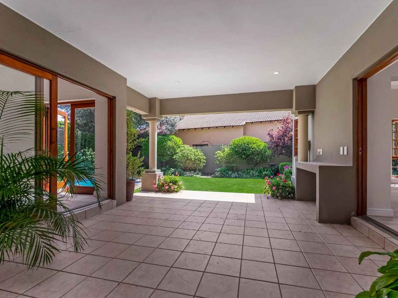 A spacious covered patio featuring tiled flooring, a built-in braai, and large sliding glass doors that open onto a well-maintained garden.