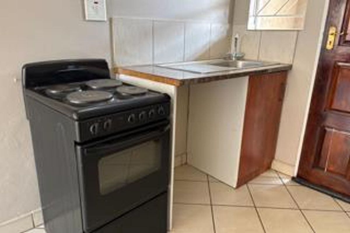 A compact kitchen area featuring a freestanding electric stove, a single basin sink with tiled splashback, and basic wooden cabinetry.
