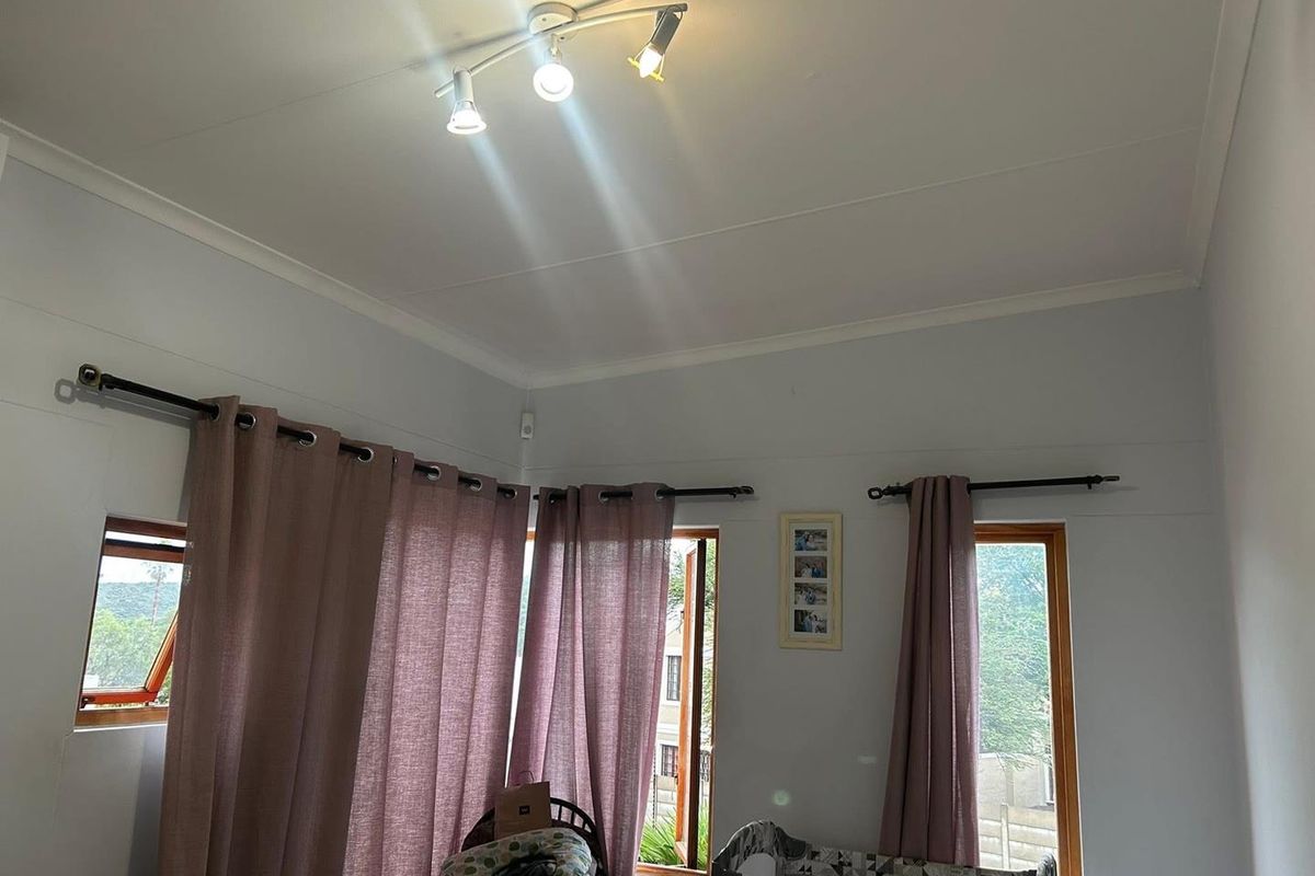 A bedroom featuring wooden window frames, curtain rods, and a ceiling-mounted spotlight fixture.