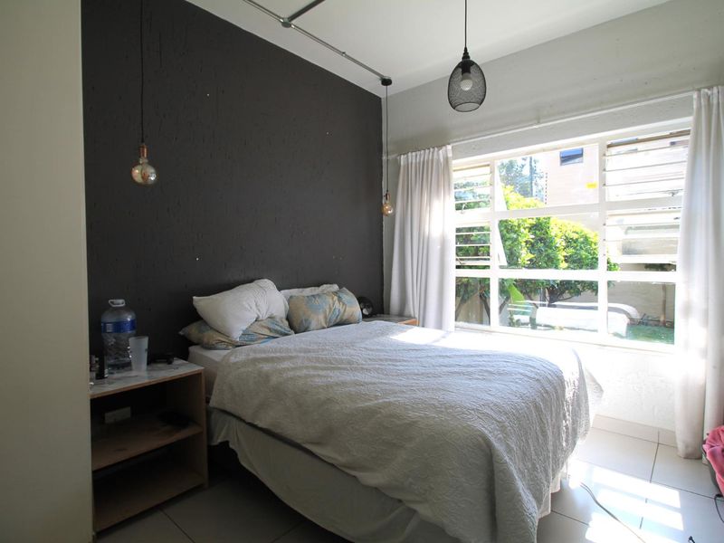 A bedroom featuring tiled flooring, a large window with natural light, and a dark accent wall with pendant lighting.