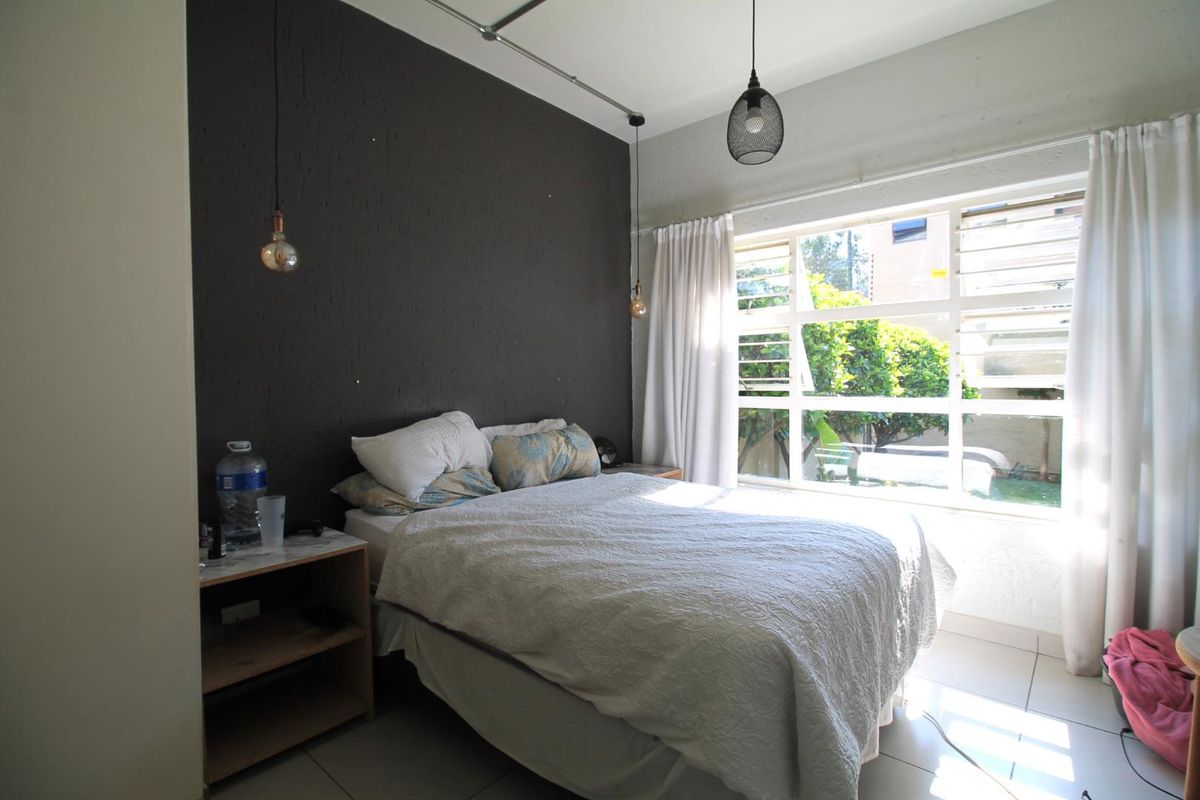 A bedroom featuring tiled flooring, a large window with natural light, and a dark accent wall with pendant lighting.