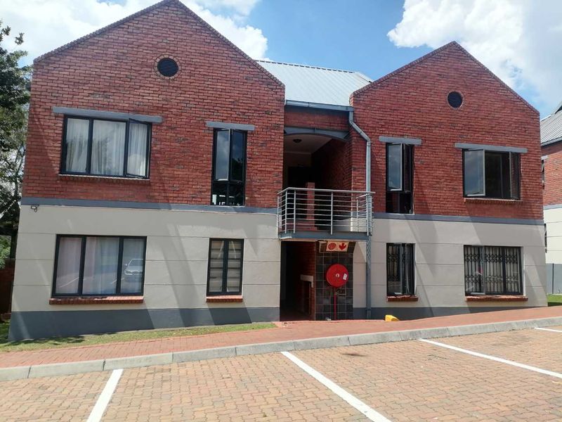 Front elevation of a two-story apartment building featuring face brick and rendered walls, metal roof, and a central balcony with paved parking in front.