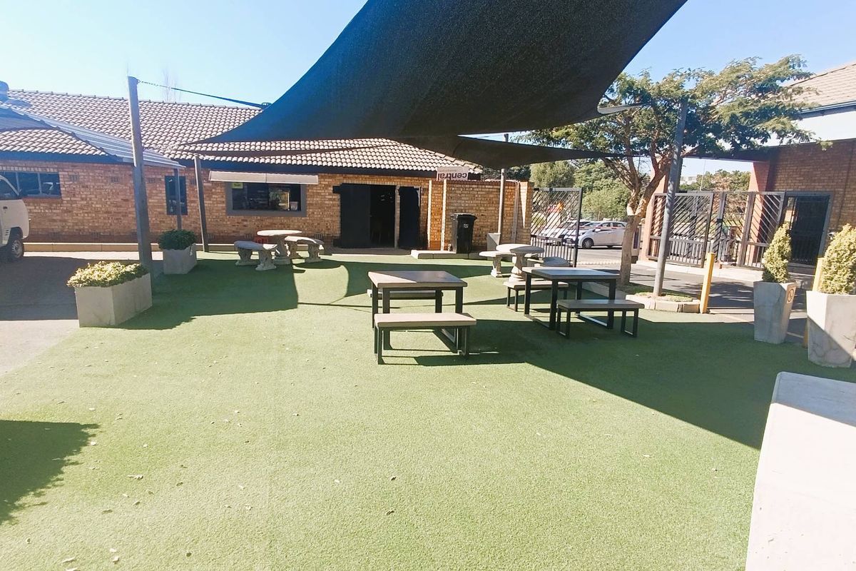 An outdoor communal area featuring artificial turf, fixed shade sails, and built-in concrete planters, providing a functional space for residents.