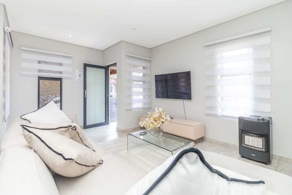 A bright and modern living room featuring tiled flooring, recessed lighting, and large windows with roller blinds, providing a clean and comfortable living space.