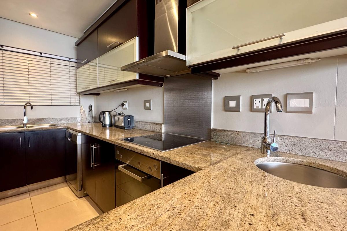 Modern kitchen featuring dark wood cabinetry, granite countertops, built-in oven, electric hob, stainless steel extractor fan, and dual sink configuration.