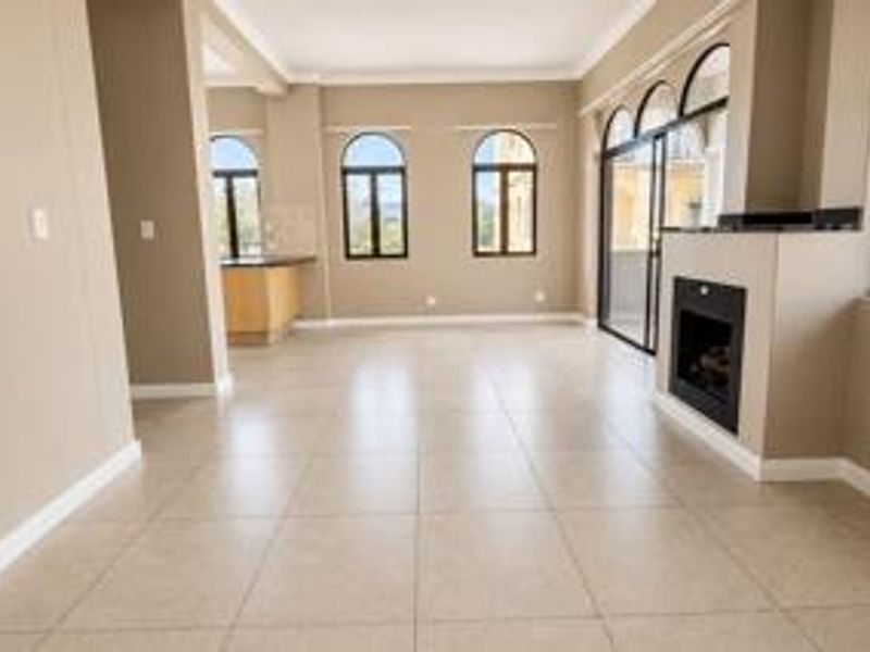 Spacious open-plan living area featuring neutral tiled flooring, a built-in fireplace, arched windows, and direct access to a balcony through sliding glass doors.