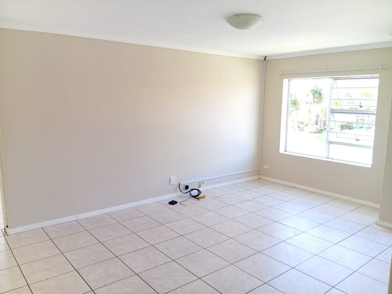A bright, empty living room featuring neutral tiled flooring, a large window, and simple ceiling lighting, ready for personalization.