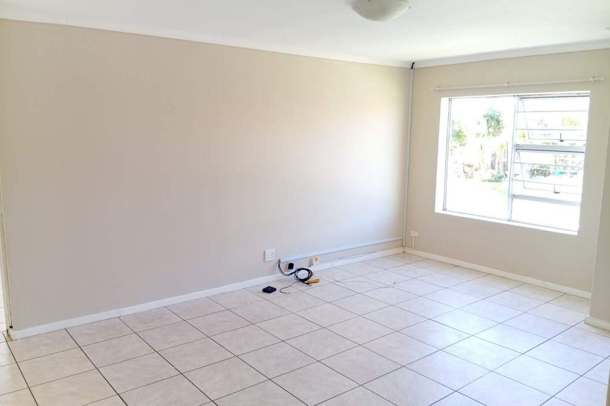 A bright, empty living room featuring neutral tiled flooring, a large window, and simple ceiling lighting, ready for personalization.
