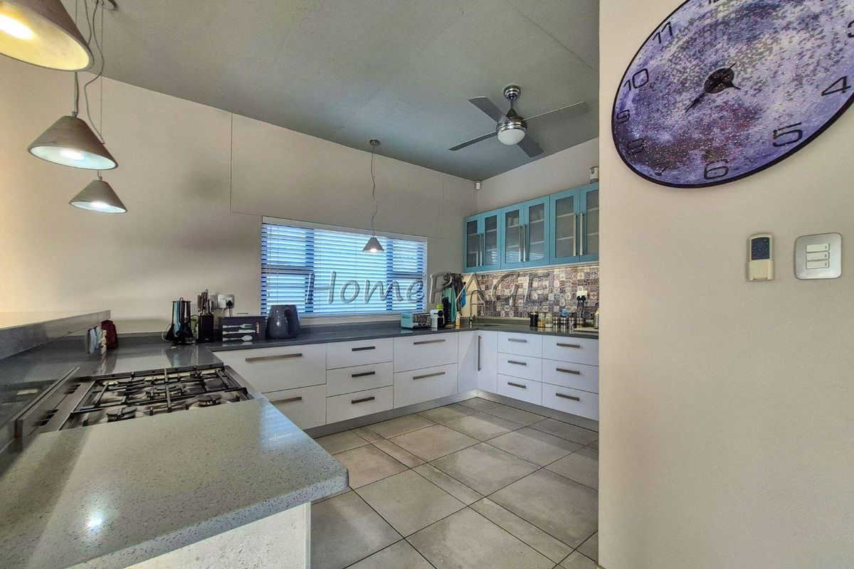 Modern kitchen featuring white and blue cabinetry, stone countertops, gas hob, mosaic backsplash, and large format floor tiles.