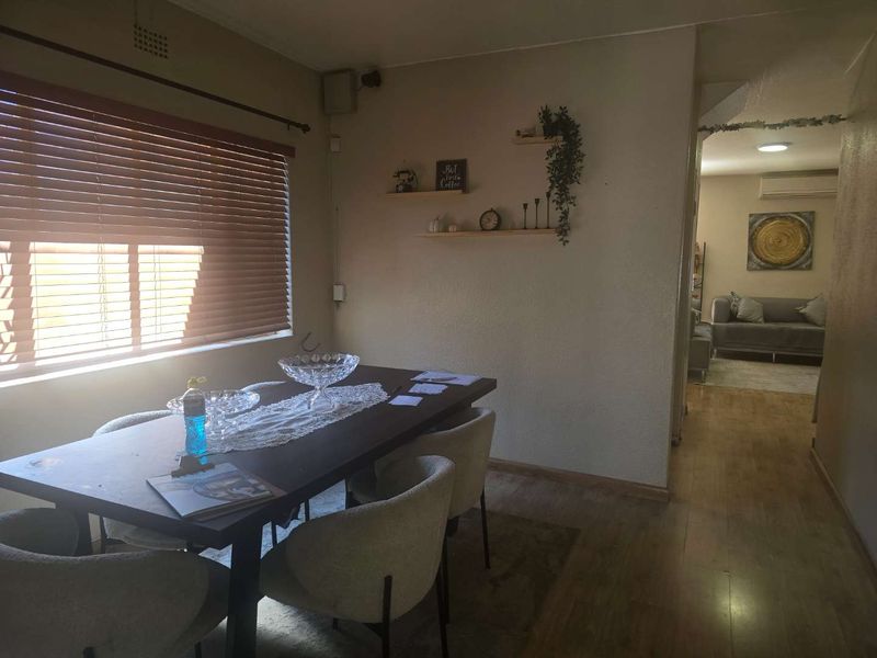 A dining room area featuring laminate flooring and venetian blinds, with an open flow leading into an adjacent living space.